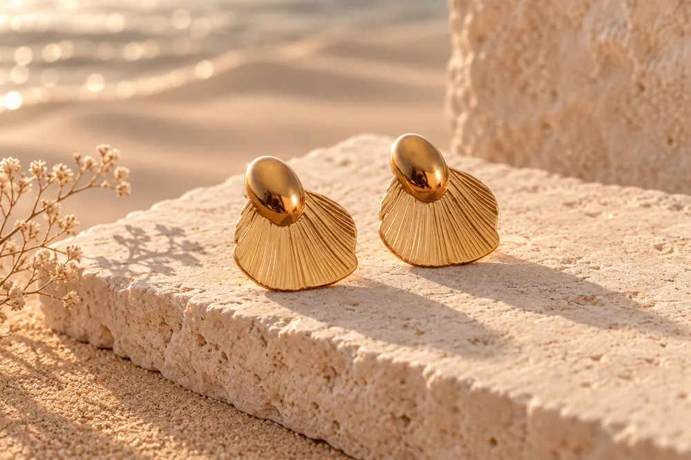 Sculptural gold-toned shell earrings in the warm light of the seaside